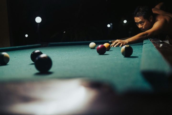 A player leaning over a green pool table at night, aiming a cue