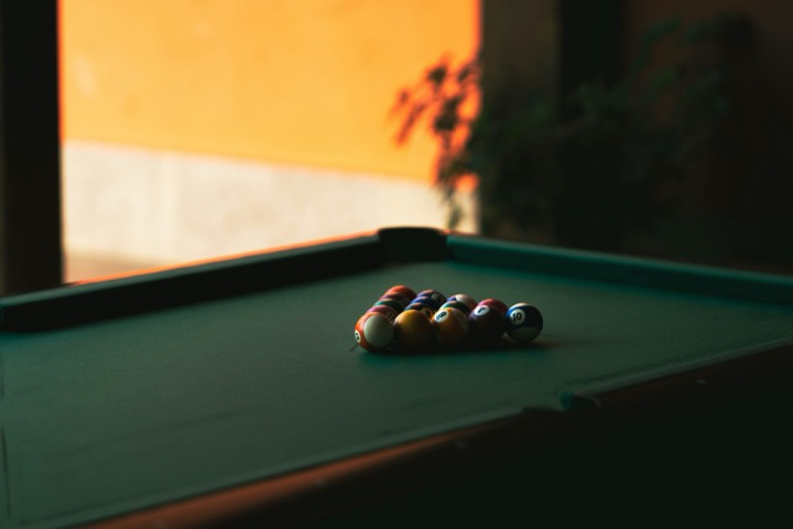 Racked pool balls on green felt in front of a sunlit orange wall