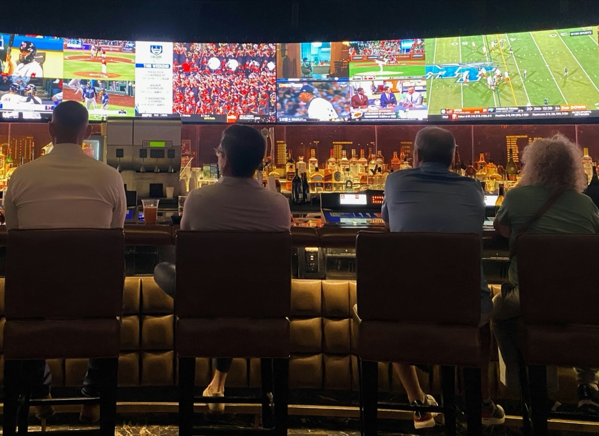 People seated at a bar facing a wall of screens showing several live sports games