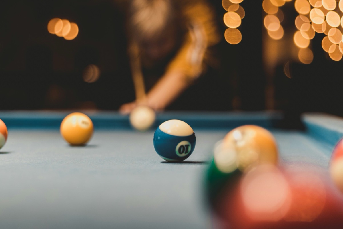 Close-up of a blue striped ten ball on a pool table, with a blurred player and warm lights behind