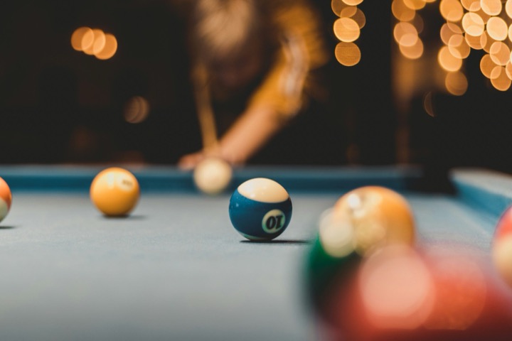 Close-up of a blue striped ten ball on a pool table, with a blurred player and warm lights behind